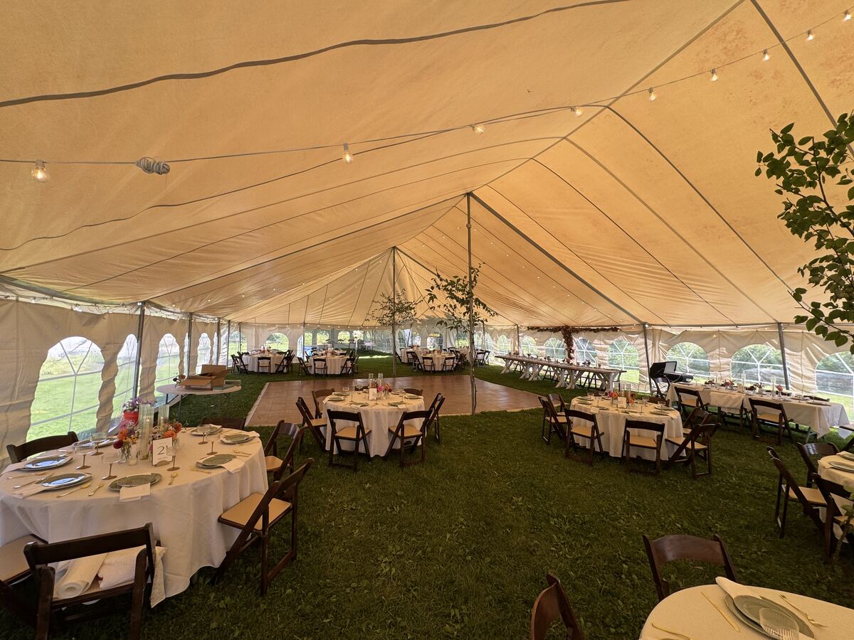 Tented wedding reception at Twin Pines with round tables set with white linens, a dance floor and string lights
